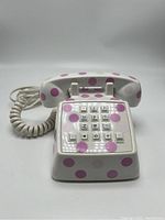 Front view of vintage mini push button phone with white base and pink polka dots, showing keypad and handset.