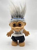 Front view of vintage Russ troll doll with gray hair, blue and white headband, white tank top with 'Aged to Perfection' text, and black shorts.
