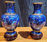 Front view of two blue cloisonné vases featuring dragon and floral designs on wooden bases, showing intricate hand-painted details.