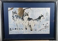 Front view of framed print showing three wolves in snowy forest scene with dark frame and blue matting