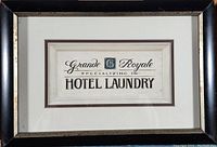 Front view of the framed print featuring the text 'Grande Royale specializing in Hotel Laundry' with the black frame and white matting.