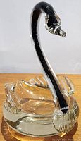 Side view of the clear glass swan figurine showing the black core running through the elegant neck and head with detailed wings and solid base.