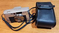 Canon SureShot Classic 120 camera front view with attached wrist strap and carrying case visible on the side.