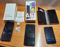 Image showing Samsung Galaxy A5 2017 box with phone, Samsung Galaxy A51 box with phone and accessories, Nokia phone in flip case, and HTC phone on wooden surface.
