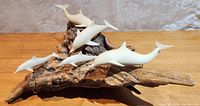 Front and side view showing six white resin dolphins mounted on a textured driftwood base with detailed grain and knots.
