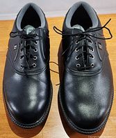 Top view of pair of black FootJoy golf shoes showing good overall condition with black laces tied.