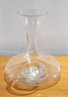 Clear glass wine aerator decanter with wide base and narrow neck seen from front on a wooden surface.
