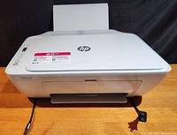 Front view of HP Deskjet 2600 All-In-One printer with power and USB cables connected, showing top panel with control buttons.