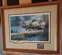Framed commemorative print showing wild geese flying over marsh landscape, including wooden frame and fabric mat with smaller inset print.