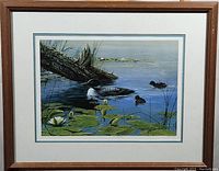 Framed print artwork showing a serene water scene with water lilies and ducks, natural setting, wooden frame.