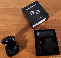 Samsung Galaxy Buds Pro earbuds in open charging case beside product box and empty packaging insert on a wooden surface.