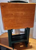 Set of four rectangular solid wood TV trays stacked vertically showing wood tops and dark green folding legs