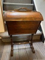 Front view of the antique walnut sewing/storage basket on its stand, showing the curved hinged lid and built-in handle.