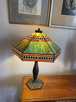 Full view of lit lamp showing hexagonal stained glass shade and bronze metal base