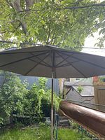 Front view of open teak umbrella with grey canvas canopy and teak pole in backyard