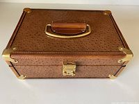 Top view of closed brown textured leather jewelry box with handle and brass corner hardware.