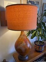 Full lamp with tangerine fabric shade in room setting showing overall shape and size.