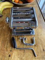 Full front view of the chrome Olympia pasta machine with clamp and crank detached and placed outward.
