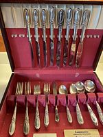 Photo showing full arrangement of the cutlery set including knives, forks, spoons, sugar spoon, butter cutter inside the red fabric-lined wooden box.