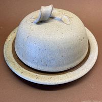 Cream-colored lidded butter dish with cinnamon speckles and a dark brown rim, shown from angled side view.