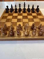 Front view of the complete chessboard with all chess pieces set up in starting position, showing the contrasting wood squares and paired dark and light pieces.