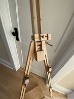 Close-up of the hardwood easel showing brass hardware and adjustable parts with signs of paint use.