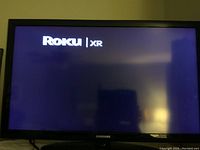 Front view of a Samsung television powered on showing the Roku XR startup screen.