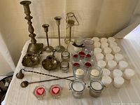 Photo showing the full assortment of vintage brass candlesticks of various heights, glass jars with candles, candle snuffers, and decorative heart-shaped candles.