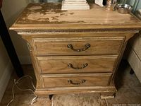 Front of wooden nightstand showing three drawers and metal handles. Noticeable wear on the top surface.