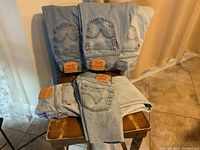 Five pairs of vintage Levi’s 505 jeans, light blue denim, displayed folded on chair and floor. Shows red Levi's tags and leather patches.