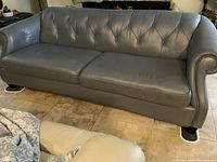 Full front view of blue-gray leather sofa with tufted back and rolled arms