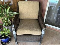 Front view of patio chair showing beige patterned cushions on woven synthetic rope material with metal frame and peeling finish on arms.