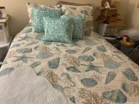 Full queen bed with reversed sea themed bedspread in blue tones, with coral pillows and matching shams