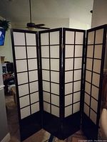 Full view of four-panel black and white wooden room divider showing grid pattern and hinges.