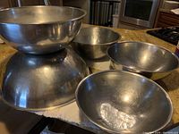 Five stainless steel mixing bowls nested and arranged on a counter, showing size variation and general condition.