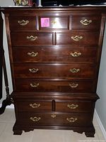 Front view of Thomasville tall boy dresser showing multiple drawers and brass handles, queen anne style base and overall finish.