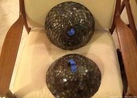 Two dome-shaped Tiffany style lamp shades placed on a chair, one with darker blue and gray mosaic glass pattern and the other similar.
