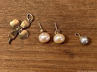 Photo showing the 10k gold flower-shaped pendant, small round pendant, and pearl stud earrings on a wooden surface.