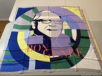 Photo showing large silk scarf with Bon Genre portrait design and color blocks including green, yellow, blue, and purple with orange text.