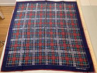 Photo of a silk scarf with navy blue border and multicolor plaid pattern featuring stitching designs and Pierre Balmain branding in the corner.