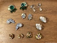 Full view of all seven pairs of clip-on earrings on wood surface showing diverse styles and colors.