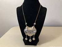 Front view of silver necklace showing detailed zodiac animal pendant with three hanging spheres on a necklace stand.