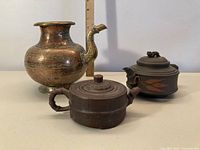 Photo showing entire lot: two Chinese clay teapots and one copper water pot with ruler for scale.
