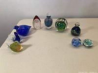 Overall view of ten art glass items including perfume bottle, paperweights, and birds arranged on table