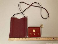 Red leather Franck Muller satchel next to red leather MCM wallet with gold-tone hardware, both placed beside a ruler showing size of satchel around 7.5 inches wide.