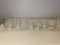 Four distinct Iittala beer mugs in a row on a table showing overall size and shape differences.