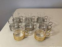 Set of 8 hot drink glasses arranged on table, showing 6 with silver holders and 2 with gold holders.
