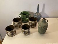 Overview of 7 ceramic items: 4 matching West German planters, green handled planter, blue vase, green jug vase, arranged on table