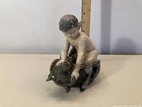 Front angle of Royal Copenhagen figurine showing boy holding down a bear with ruler background for scale.
