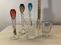 Five glass items displayed on table with ruler for scale: three signed colorful Orrefors vases with spiral designs inside stems and two clear glass oil burners, one with cut diamond pattern.